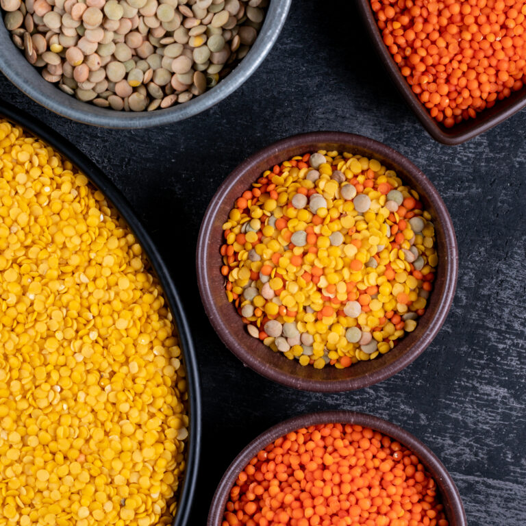 Close-up green, red and yellow lentils in different colored bowls and black pan on black stone background. vertical